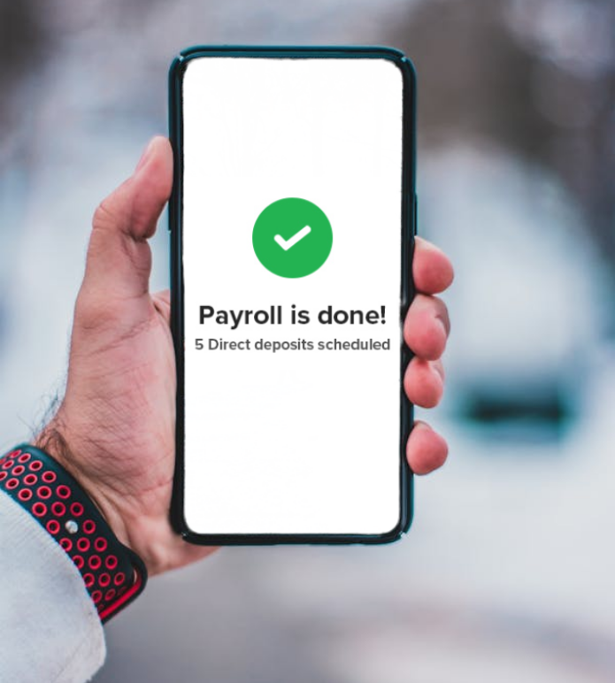 Hand holding a smartphone showing a payroll confirmation screen with a green checkmark and message that direct deposits are scheduled for home care staff.