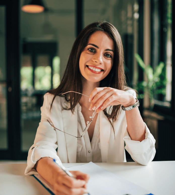 Smiling HR professional holding glasses and pen, seated at desk with time tracking documents